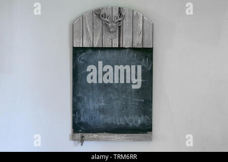 Schwarze und weiße Leere rustikalen Holzmöbeln Schiefertafel mit Kopieren und Schnitzen der Kopf einer Hirsche mit geweihen auf einer weißen Wand Stockfoto