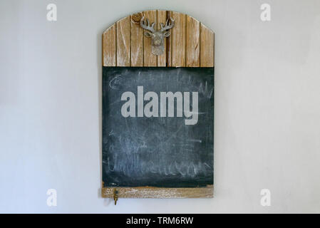 Leer Landhausstil Schiefertafel mit Kopieren und Schnitzen der Kopf einer Hirsche mit geweihen auf einer weißen Wand Stockfoto