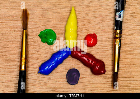 Eine primäre und sekundäre Farbe Rad aus Blobs der Acrylfarbe mit zwei Bürsten einsatzbereit Artist's, alle auf einem Holzboden. Farben sind sehr v Stockfoto