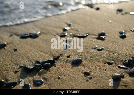 Nassen Kieselsteinen am Strand in der Abendsonne. Sea Wave auf Seeküste mit runden Steinen. Stockfoto