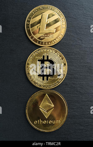 Physische Bitcoin, Litecoin und des Astraleums Gold Münzen auf einen schwarzen Stein Schiefer platte Hintergrund. Cryptocurrency. Vertikale Ausrichtung. Stockfoto