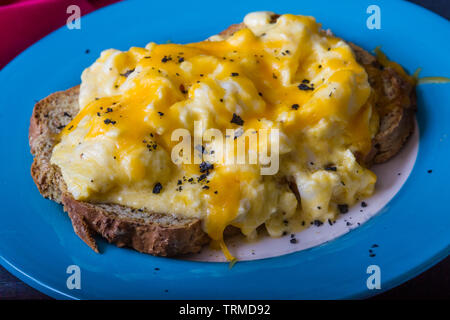 Rührei mit geschmolzenem geriebenen Käse auf Toast, Frühstück oder Brunch, gekrönt mit Holzkohle Salz Stockfoto