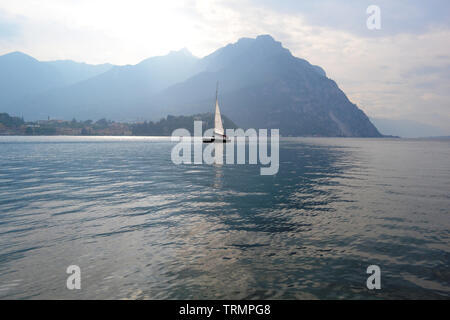 Schöner Panoramablick in die Hintergrundbeleuchtung an den Comer See in Lecco mit Segelboot Navigation von der Stadt bei Sonnenuntergang im Frühjahr. Stockfoto