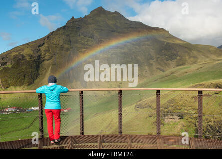 Frau auf der Suche nach ein Regenbogen über dem Wasserfall Skogafoss in Island Stockfoto