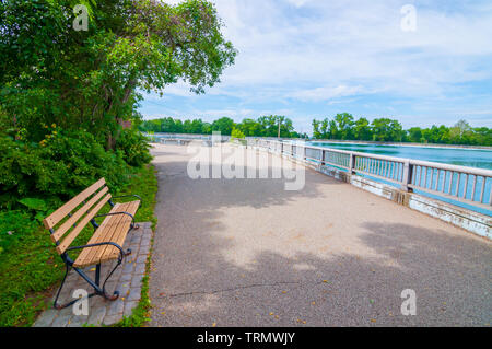 Ein Gehweg rund um die Highland Park Reservoir an einem strahlenden Frühlingstag mit einer Bank im Schatten in Pittsburgh, Pennsylvania, USA Stockfoto