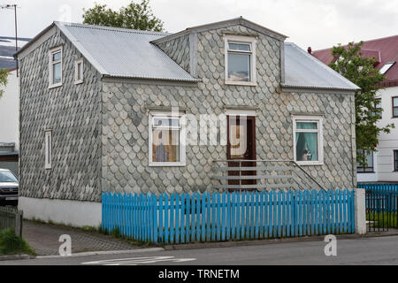 Akureyri, North Island. Ein altes Haus mit abgerundeten Schiefer Schindeln in einen Fisch Skala Muster bedeckt, mit einem blauen Garten Zaun vor Stockfoto