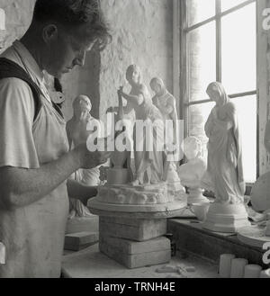 1950, historische, eine männliche Handwerker stehen durch ein Fenster in einer Töpferei und Keramik studio, Arbeiten auf weibliche Figuren oder Statuetten, England, UK. Stockfoto