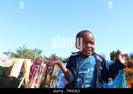 Ein kleiner Junge spielt, während seine Eltern Souvenirs irgendwo in Südafrika verkaufen Stockfoto