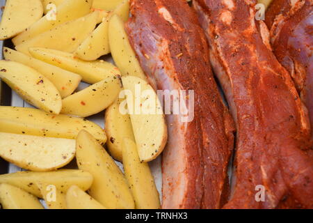 Saftige Rippchen gewürzt mit organischen ungekocht Potato Wedges auf einem silbernen Flachbild Backblech Stockfoto