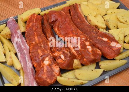 Saftige Rippchen gewürzt mit organischen ungekocht Potato Wedges auf einem silbernen Flachbild Backblech Stockfoto