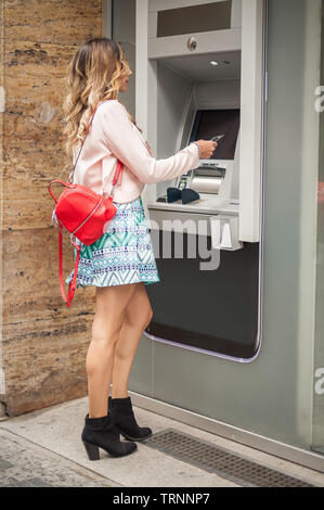 Junge Frau nimmt Geld an einem Geldautomaten. Finanzen, Kreditkarte, Entzug von Geld. Ergreift eine Karte vom Geldautomaten Stockfoto