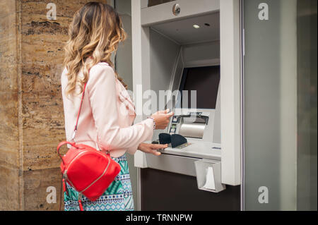 Junge Frau nimmt Geld an einem Geldautomaten. Finanzen, Kreditkarte, Entzug von Geld. Ergreift eine Karte vom Geldautomaten Stockfoto