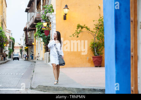 Schöne Frau im weißen Kleid allein an der bunten Straßen der kolonialen Stadtmauer von Cartagena de Indias Stockfoto