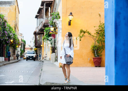 Schöne Frau im weißen Kleid allein an der bunten Straßen der kolonialen Stadtmauer von Cartagena de Indias Stockfoto