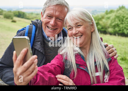 Lächelnd Senior Paar Wandern in der Landschaft stehend durch Tor und unter Selfie auf Handy Stockfoto
