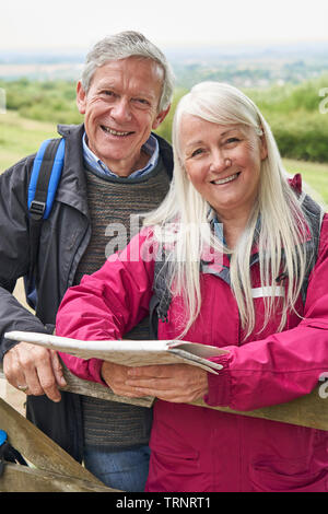 Portrait von lächelnden Senior Paar mit Karte Wandern in der Landschaft stehend von Gate Stockfoto