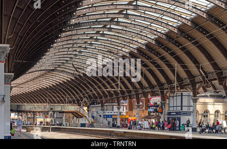 Der Bahnhof York mit seiner aufwendigen 19 Architektur und geschwungene Vordach. Geschäfte, Cafés und Passagiere sind auf den Plattformen. Stockfoto