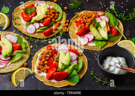 Vegan Tacos mit gebackenen Kichererbsen, Avocado, Soße und Gemüse auf einem dunklen Hintergrund. Stockfoto