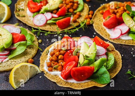 Vegan Tacos mit gebackenen Kichererbsen, Avocado, Soße und Gemüse auf einem dunklen Hintergrund. Stockfoto