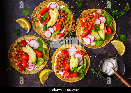 Vegan Tacos mit gebackenen Kichererbsen, Avocado, Soße und Gemüse auf einem dunklen Hintergrund. Stockfoto