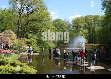 Besucher zum Keukenhof Gardens in der Nähe von Lisse in Südholland, Niederlande Kreuzung große Trittsteine durch eine Wasserfontäne in der zierteich. Stockfoto