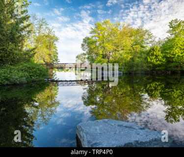 Einen schönen Frühling Morgen Schuß des Beavermead park Fußgängerbrücke und Reflexion, über die perfekt noch Wasser eines Zweiges der Otonabee Rive Stockfoto