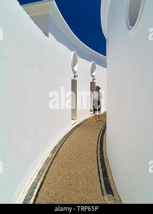 Rhodes, Griechenland - 07/26/2008: Frau gehen auf Kieselsteinen Boden, innen oder Kalithea Kalithea Quellen Therme Räumlichkeiten. Korridor zwischen weißen Gebäude. Stockfoto