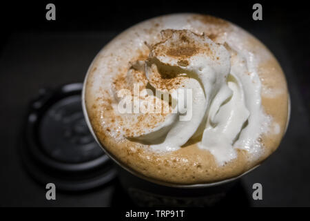 Blick von oben auf einen heißen Kaffee im Pappbecher mit Sahne und Schokolade Pulver topping vor einem dunklen Hintergrund. Stockfoto