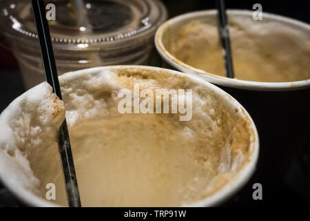 Verbrauchte heißen Kaffee Pappbecher mit über Sahne und Schokolade topping vor einem dunklen Hintergrund. Stockfoto