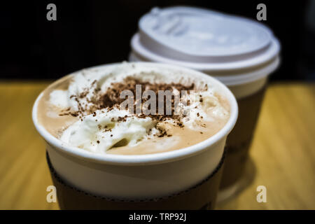 Hot mokka Kaffee im Pappbecher mit Sahne und Chocolate Chip Topping auf einem holztisch vor einem schwarzen Hintergrund. Stockfoto
