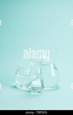 3 transparentes Glas Vasen mit klarem Wasser auf einem türkis Hintergrund gefüllt. Spiel von Licht und Transparenz. Minimale noch leben Farbe Fotografie Stockfoto