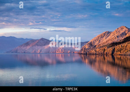 Sonnenlicht bei Sonnenaufgang auf den felsigen Hügeln der Bucht Baska und der Insel Prvić. Adria. Kroatien. Europa. Stockfoto