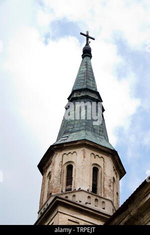 Turm mit spitzen Cooper grüne Dach eines alten verwitterten katholische Kirche in Ecka, Serbien, aus der Nähe gegen bewölkter Himmel Stockfoto