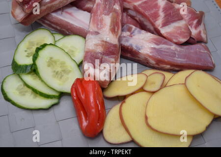 Organische rohe Schweinerippchen auf eine Küche, die mit frischen runden Scheiben geschnittenen Gemüse Stockfoto