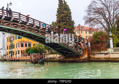 Venedig an einem regnerischen Tag, an dem die Menschen über den Canal Grande durch eine Brücke mit bunten Sonnenschirmen Stockfoto