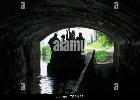 Ansicht der Rückseite des Menschen in UK narrowboat auf britischen Kanal bewegen durch dunkle Tunnel Silhouette; auf den Kopf Mann, Beine in die Luft, treibt Boot von Leggings. Stockfoto