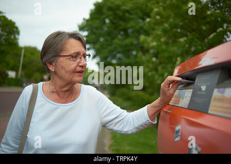 Glückliche und Gesunde ältere Frau, einen Brief in einen roten Briefkasten draußen im hellen Sommer Sonnenschein Stockfoto