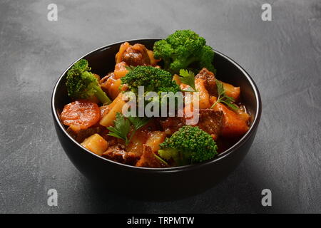 Traditionelle hausgemachte Ungarische Rindfleisch Eintopf, Gulasch mit Kartoffeln, Karotten, Tomaten, Brokkoli in eine Schüssel geben. Stockfoto