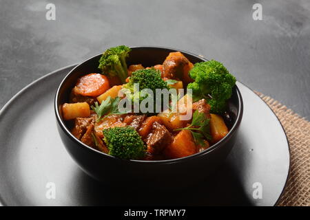 Traditionelle hausgemachte Ungarische Rindfleisch Eintopf, Gulasch mit Kartoffeln, Karotten, Tomaten, Brokkoli in eine Schüssel geben. Stockfoto