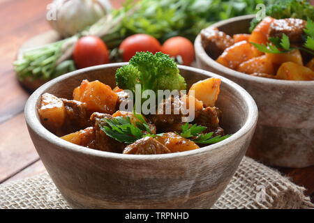 Traditionelle hausgemachte Ungarische Rindfleisch Eintopf, Gulasch mit Kartoffeln, Karotten, Tomaten, Brokkoli in eine Schüssel geben. Stockfoto