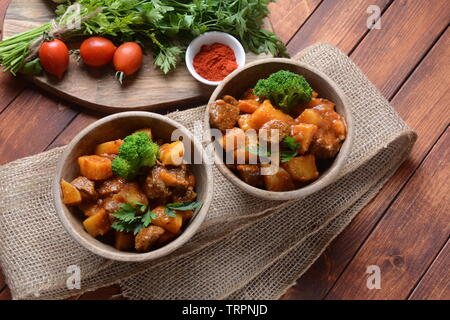 Traditionelle hausgemachte Ungarische Rindfleisch Eintopf, Gulasch mit Kartoffeln, Karotten, Tomaten, Brokkoli in eine Schüssel geben. Stockfoto