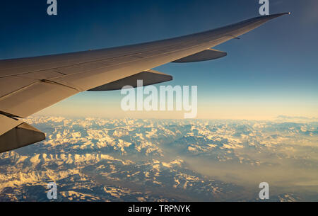 Flügel des Flugzeugs über Berg Abdeckung mit weißen Schnee. Flugzeug fliegen auf blauen Himmel. Blick aus dem Flugzeug Fenster. Commercial Airline Flight. Flugzeug Stockfoto