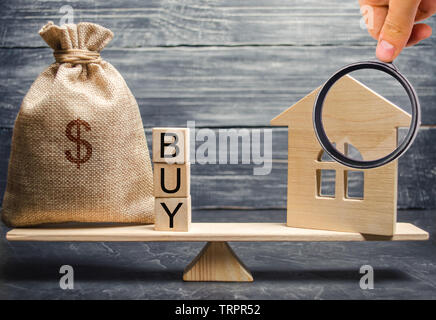 Eine Geld-Beutel und Holzklötze mit dem Wort kaufen und eine Miniatur Haus auf einer Waage. Die Anhäufung von Geld für den Kauf von Immobilien. Der Kauf einer Uhr Stockfoto