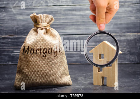 Ein Beutel mit Geld und das Wort Hypothek und ein Holzhaus. Die Anhäufung von Geld Zinsen auf Hypotheken zu bezahlen. Kauf einer Immobilie in der Schuld. Ta Stockfoto