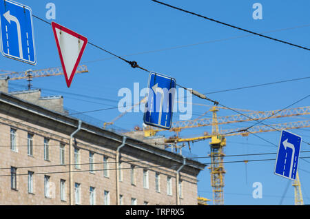 Verkehrszeichen 'Nach links' und 'Weichen' im Hintergrund Baukräne und blauer Himmel Stockfoto