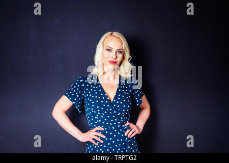 Studio Portrait von schöne blonde Frau in einem dunkelblauen Kleid gegen Schwarze einfachen Hintergrund Stockfoto