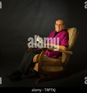 Eine achtzigjährige Dame in einem Schaukelstuhl mit einem Buch sitzen Stockfoto