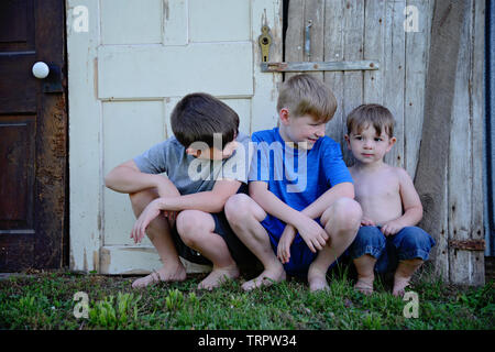 Drei Jungs sitzen durch alte verwitterte Holz Türen Stockfoto