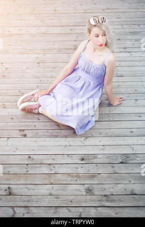Junge Frau sitzt auf der Holzterrasse im Sommer Kleid Stockfoto