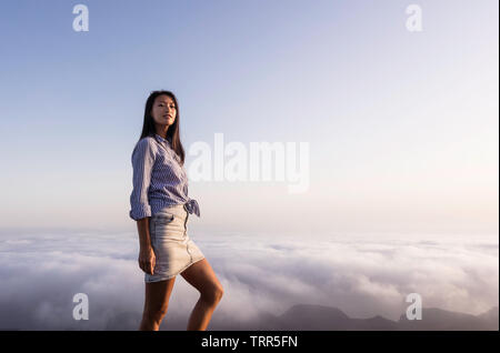 Porträt einer Frau, die auf einem Berg über den Wolken bei Sonnenuntergang Stockfoto